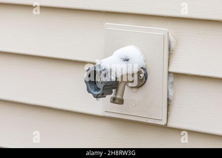 Outdoor water spigot covered in snow during winter. Home repair, maintenance and weatherproofing concept Stock Photo