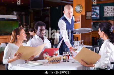 Polite waiter bringing ordered drinks to restaurant guests Stock Photo