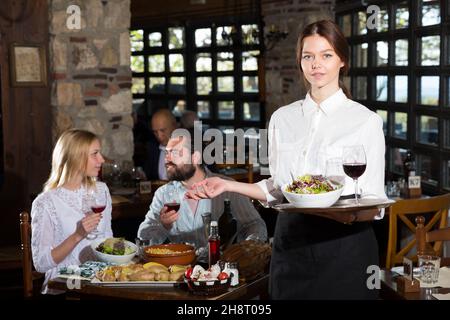 Positive woman waiter demonstrating country restaurant to visitors Stock Photo