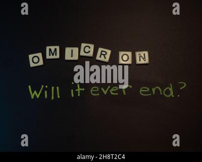 The word Omicron spelled out with off white tiles and black letters on a black background. Phrase will it ever end handwritten below.Image has copy sp Stock Photo