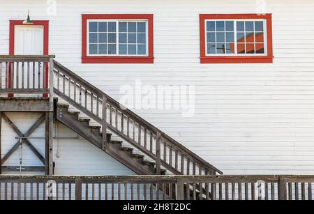 Wooden white house entrance with red windows and door with rustic wooden staircase in British Columbia Stock Photo