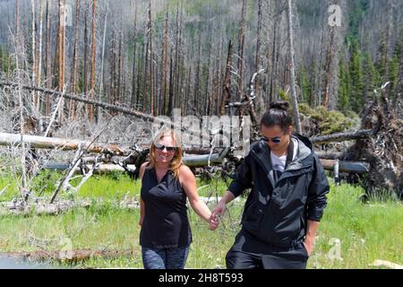 mixed race couple holding hands laughing, walking towards camera with green grass and trees behind them Stock Photo