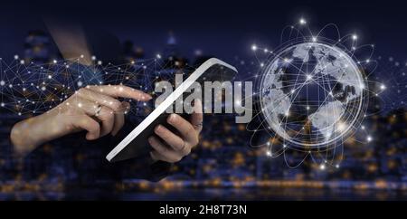 Global connection concept. Hand touch white tablet with digital hologram world, earth, map, globe sign on city dark blurred background. International