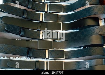 Various types of black leather belt in a row for display and sale on the market. Realistic leather belts set with metal buckles. Clothing store, shelf Stock Photo