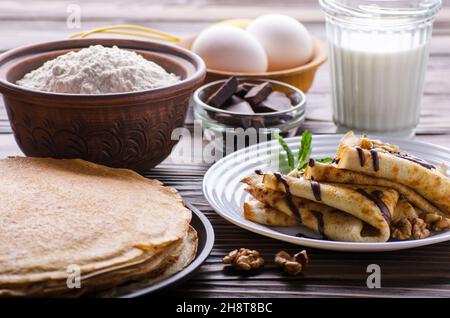 French crepes with chocolate sauce walnuts eggs and flour on wooden kitchen table Stock Photo
