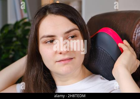 A woman sits in a chair with a massage pillow and does a neck massage. Stock Photo