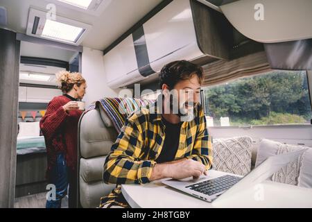 Alternative nomad lifestyle office workstation people. Man working on laptop computer inside luxury van during vacation or alternative digital lifesty Stock Photo