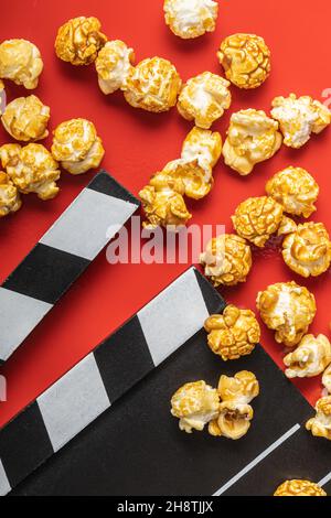 Sweet caramel popcorn and clapper board on red background. Top view. Stock Photo