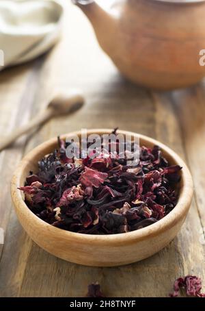 Dry hibiscus leaves in a wooden bowl on a wooden table, preparation for tea. Rustic style. Dried rosella or Sudanese rose flowers. It is very popular Stock Photo