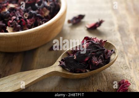 Dry hibiscus leaves lie in a wooden spoon on a wooden table, preparing for tea. Rustic style. Dried rosella or Sudanese rose flowers. It is very popul Stock Photo