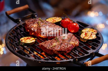 High angle of delectable beef steaks placed near zucchini and tomatoes being grilled on barbecue grid Stock Photo