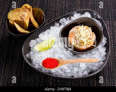 fresh salmon tartare, raw minced salmon fillet with capers and chopped onion in a bowl on ice bed, served with raw yolk, red caviar and potato chips, Stock Photo