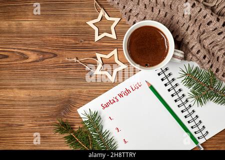 Santa's Wish List at notepad and coffee cup, scarf, fir branches on wooden background Stock Photo