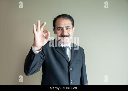 Smart mature older business man with moustache showing a OK sign with his hand wearing suit and tie Stock Photo