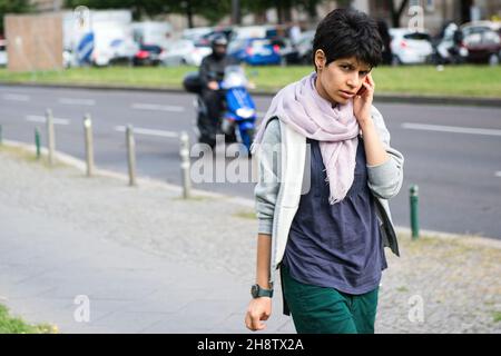 Berlin, Germany. Young adult dark haired woman  walking by while performing a mile call. Stock Photo