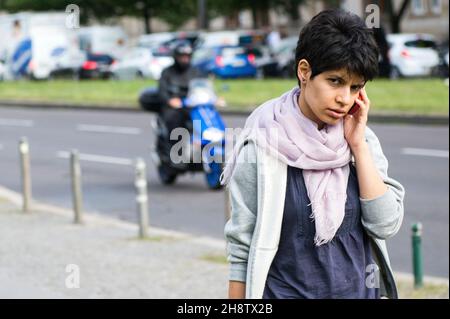 Berlin, Germany. Young adult dark haired woman  walking by while performing a mile call. Stock Photo