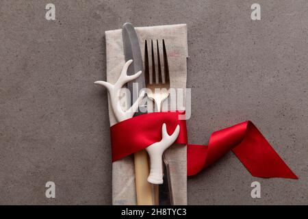 Festive Christmas table setting with cutlery wrapped in a red ribbon with an antler decoration Stock Photo