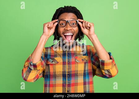 Photo of impressed pretty dark skin guy dressed checkered arms glasses open mouth isolated green color background Stock Photo