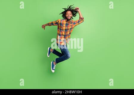 Photo of funky charming dark skin man wear plaid shirt smiling jumping high hurrying isolated green color background