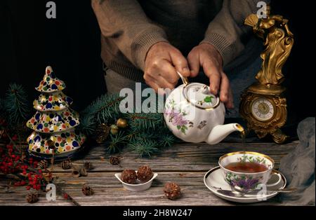 Tea ceremony with Christmas teapot and tea cup, sweets in a ceramic plate, Christmas tree branches, ceramic Christmas tree and an antique clock on woo Stock Photo