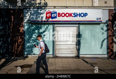 Man using his mobile, walking past a closed book shop in Rotherham Stock Photo
