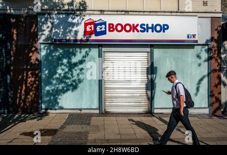 Man using his mobile, walking past a closed book shop in Rotherham Stock Photo