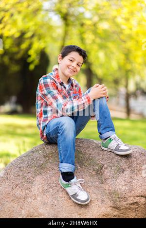 Smiling boy wearing casual clothes while sitting on rock at city park Stock Photo