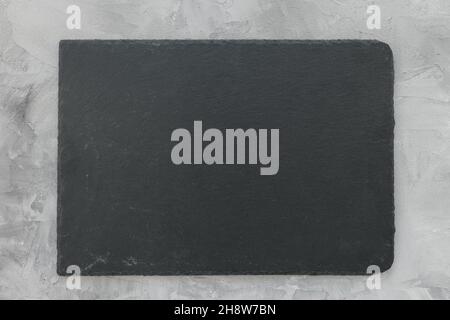 Slate plate on gray stone texture background. Kitchen stone tray for serving food. Black granite rectangle board. Empty space for menu or recipe. Top view copy space, mockup Stock Photo