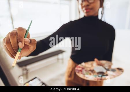 Young female painter drawing on a canvas with a paintbrush. Creative young woman holding a palette while working on a painting. Artistic female freela Stock Photo