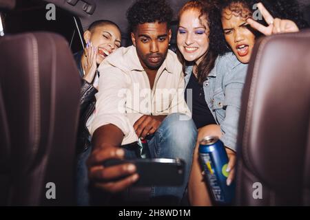 Diverse group of friends taking a selfie together inside a car. Group of young friends posing for a group photo in front of a camera phone. Carefree f Stock Photo