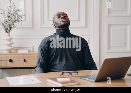 Exhausted home office employee African american male sitting with eyes closed throwing his head back Stock Photo