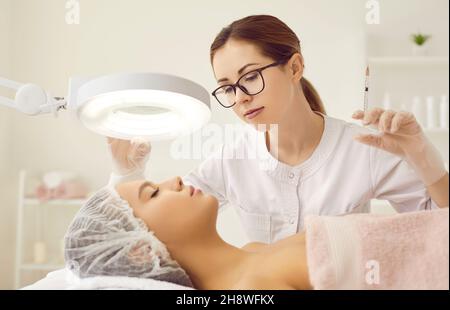 Nurse at clinic of aesthetic medicine giving beauty injection to woman under magnifying lamp Stock Photo