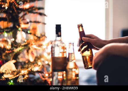 Christmas party with alcohol bottles. New year's celebration. Beer, wine and vodka. Festive Xmas tree. Alcoholism and drinking problem concept. Stock Photo