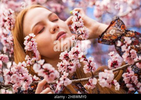 Beauty teen girl posing near blossom cherry tree with pink flowers. Spring park Stock Photo