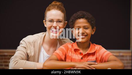Portrait of smiling redhead teacher sitting with afro student in classroom Stock Photo