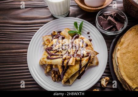 French crepes with chocolate sauce walnuts eggs and flour on wooden kitchen table Stock Photo