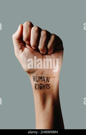 closeup of the raised fist of a man with the text human rights written in his wrist, on a gray background Stock Photo