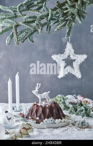 Tasty sweet chocolate bundt cake decorated with deer served on decorated table with candles on gray background in room with coniferous branches during Stock Photo