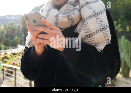 Crop stylish male in fashionable outfit using smartphone near metal railing in tropical park Stock Photo