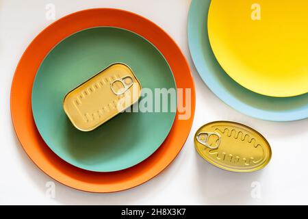 From above of rectangular closed tin can placed on green and orange round plates on white table Stock Photo