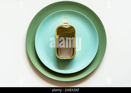 Top view of opened empty metal can with pop up lid placed on blue ceramic plate served on white table with silver fork and knife Stock Photo