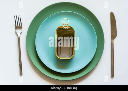 Top view of opened empty metal can with pop up lid placed on blue ceramic plate served on white table with silver fork and knife Stock Photo