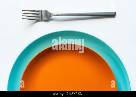 From above of round orange and blue minimalist ceramic plates placed on each other near silver fork on white table Stock Photo