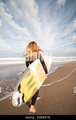 From below of female in stylish outfit standing on balcony of modern building with geometric elements on windows while using tablet near glass railing Stock Photo