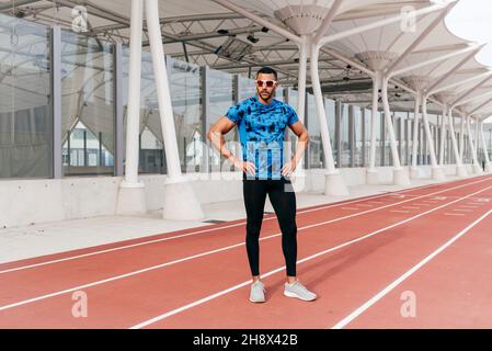 Confident athletic man with sports clothes and sunglasses standing on the running track Stock Photo