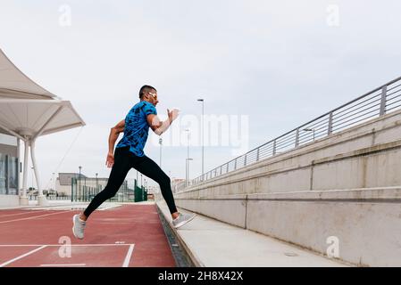 Side view of athletic man with sportswear and sunglasses exercising on the field track Stock Photo