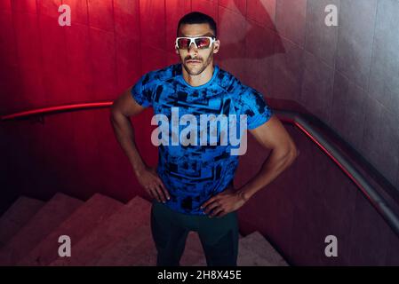 Concentrated young black athlete with sports clothing and sunglasses standing on the stairs before competition and looking at camera Stock Photo