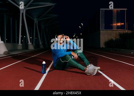 Young african athlete using phone and listening music on the floor of the running track Stock Photo