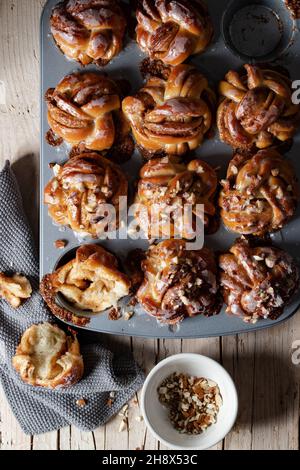 Top view pile of tasty freshly baked homemade cinnamon buns placed on wooden table with ground nuts in light kitchen Stock Photo