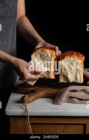Unrecognizable crop baker taking split halves of sandwich bread from grill tray located on counter in dim light Stock Photo